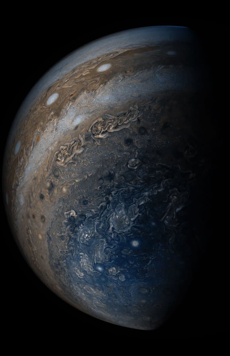 A close-up view of the planet Jupiter, highlighting its swirling cloud bands, storms, and atmospheric features against the blackness of space. The image shows the planet in a crescent phase, with the right side fading into shadow.