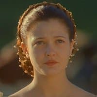 A close-up portrait of a young woman with brown hair pulled back by a beaded headband, looking directly at the camera with a neutral expression.