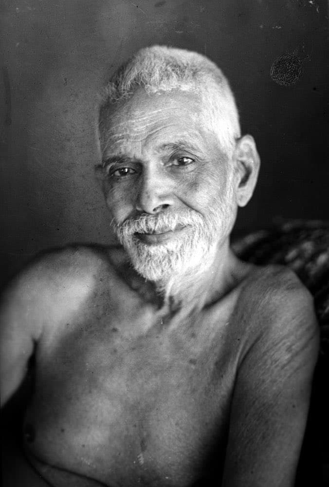 A black-and-white portrait photograph of an elderly, bare-chested man with white hair and a beard, smiling gently at the camera. The image is a historical photograph, not a text-bearing document or meme.