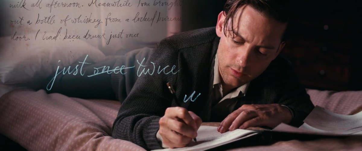 A man in a dark sweater is lying on a bed, writing in a notebook with a pen. The image features a text overlay in a cursive font that reads "just once twice" and includes a small "u" symbol.