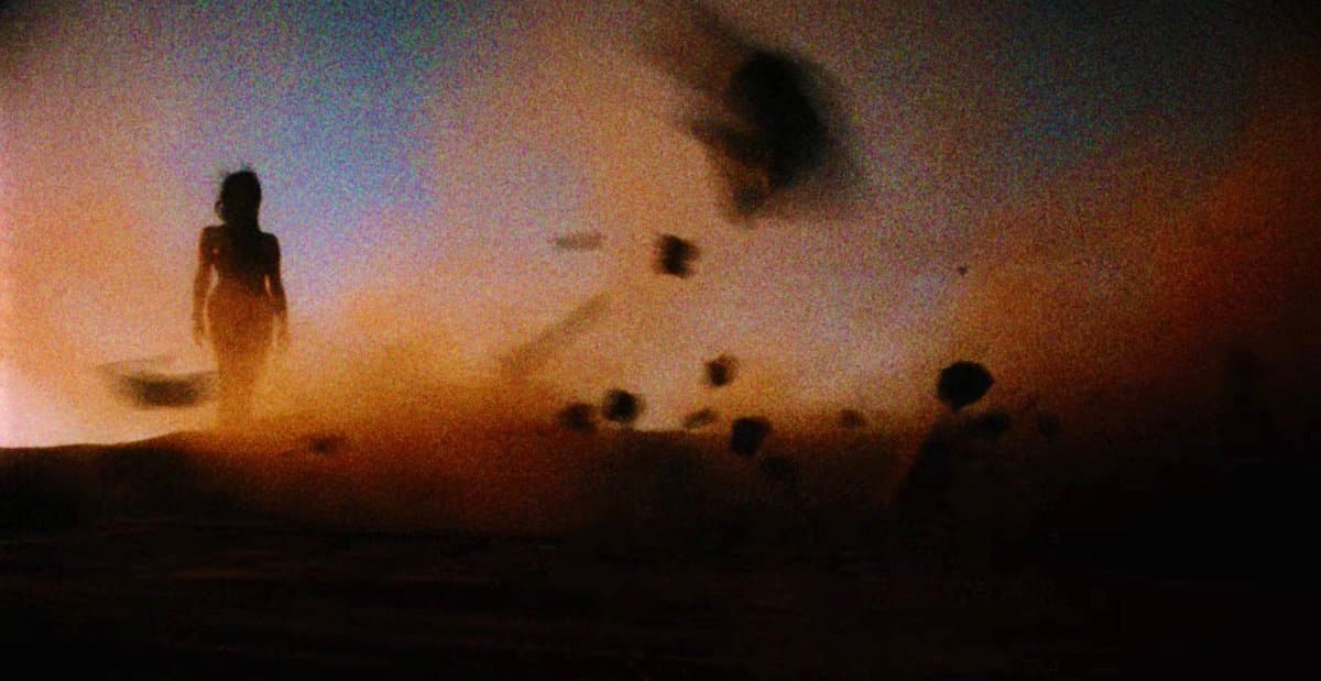 A still from the film 'The Other Side of the Wind' showing a silhouetted figure standing in a hazy, backlit landscape with dust or smoke swirling in the air.
