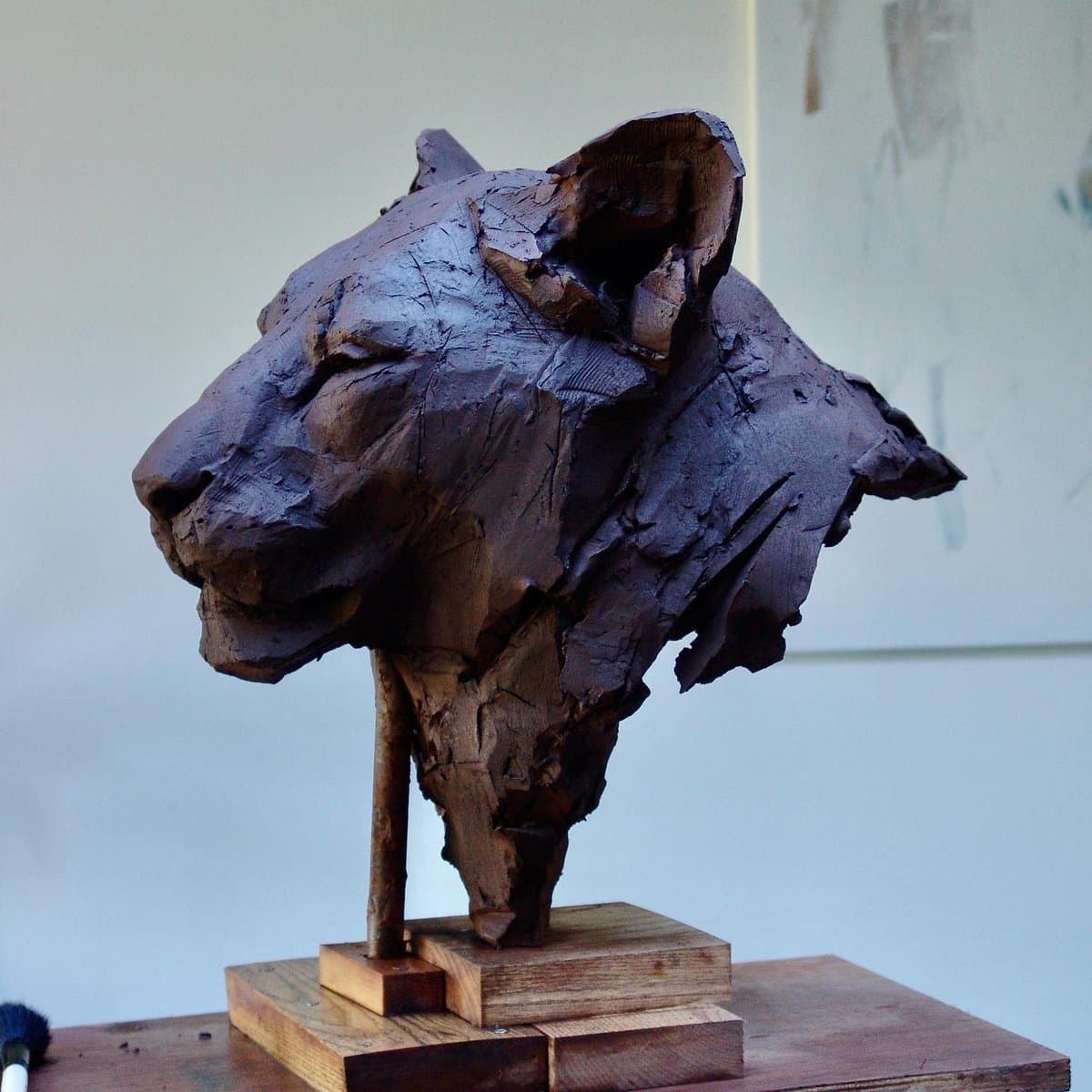 A photograph of a rough, brown clay sculpture of a lioness's head mounted on a wooden stand. The piece is titled 'Sekhmet' and was created by artist Nichola Theakston.