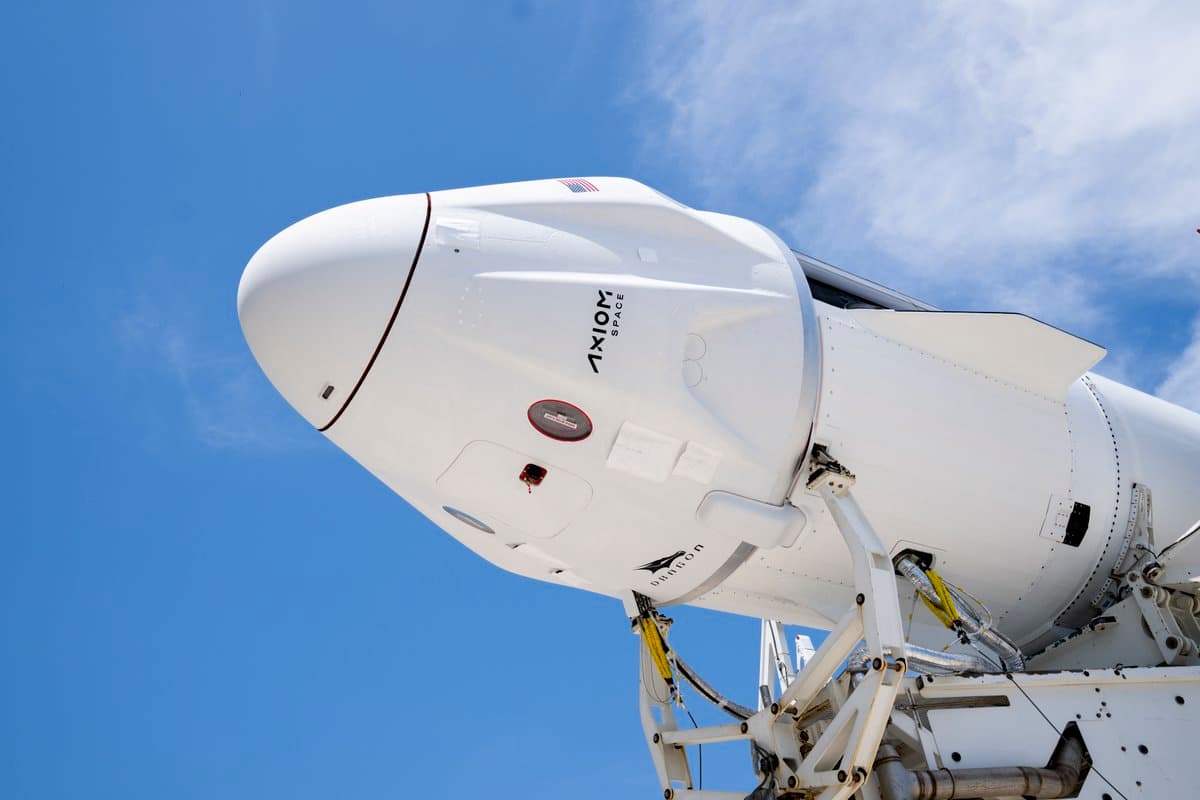 A low-angle photograph of a white SpaceX Falcon 9 rocket and Dragon capsule on a launch pad against a blue sky. The capsule features the Axiom Space logo and an American flag.