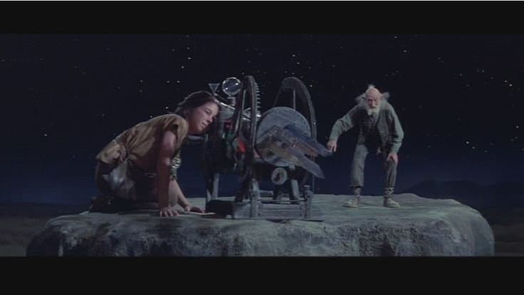A still from a movie showing a woman and an older man standing on a rocky outcrop at night, looking at a large, complex mechanical device resembling a telescope or astrolabe.