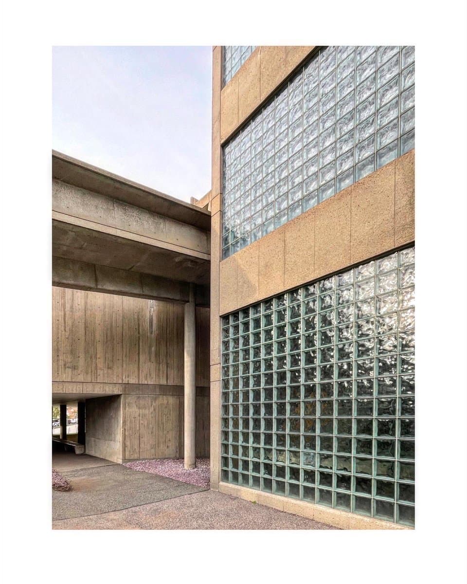A photograph of the exterior of the Carpenter Center for the Visual Arts, showcasing its distinctive Brutalist architecture with raw concrete walls and large sections of textured glass block windows.