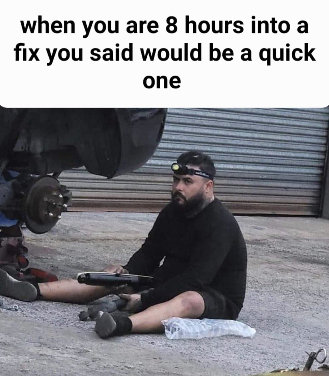 A meme image showing a man sitting on the ground next to a car that is lifted on a jack, with a headlamp on his head and a tool in his hand. The image is used to humorously illustrate a situation that has taken much longer than expected.
