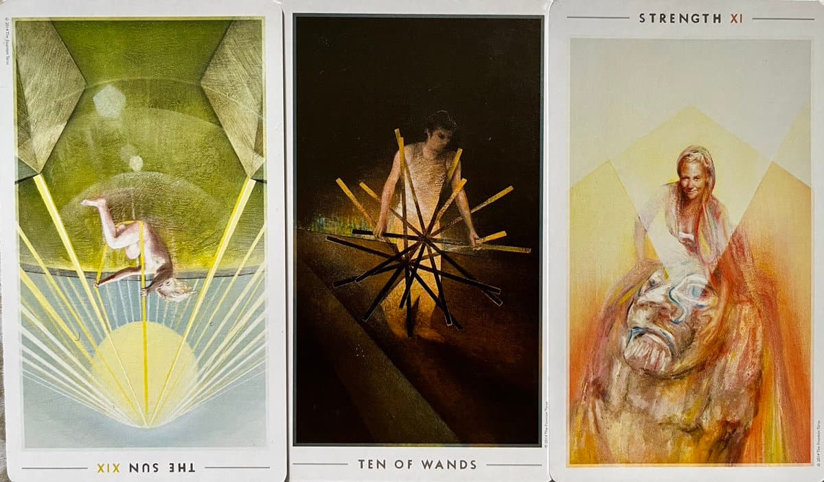 A photograph of three tarot cards laid side-by-side, showing The Sun (reversed), Ten of Wands, and Strength. The cards feature artistic illustrations of a figure, a person carrying a bundle of sticks, and a woman with a lion, respectively.