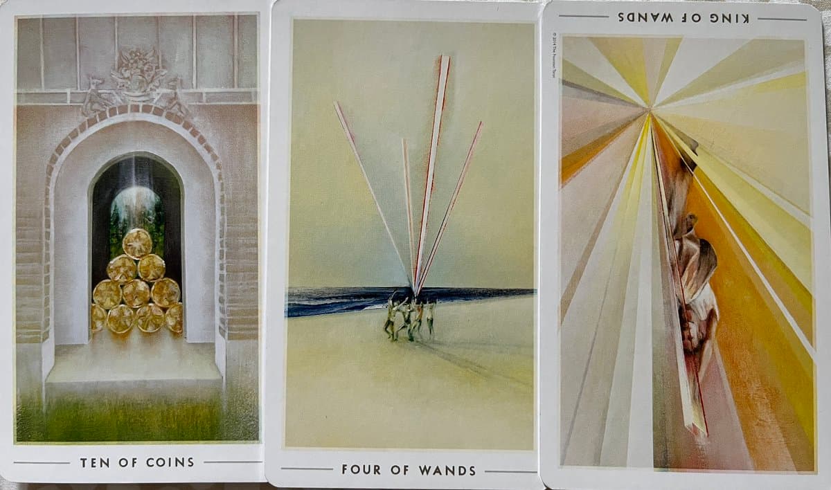 A photograph of three tarot cards laid side-by-side: the Ten of Coins, the Four of Wands, and the King of Wands (reversed).