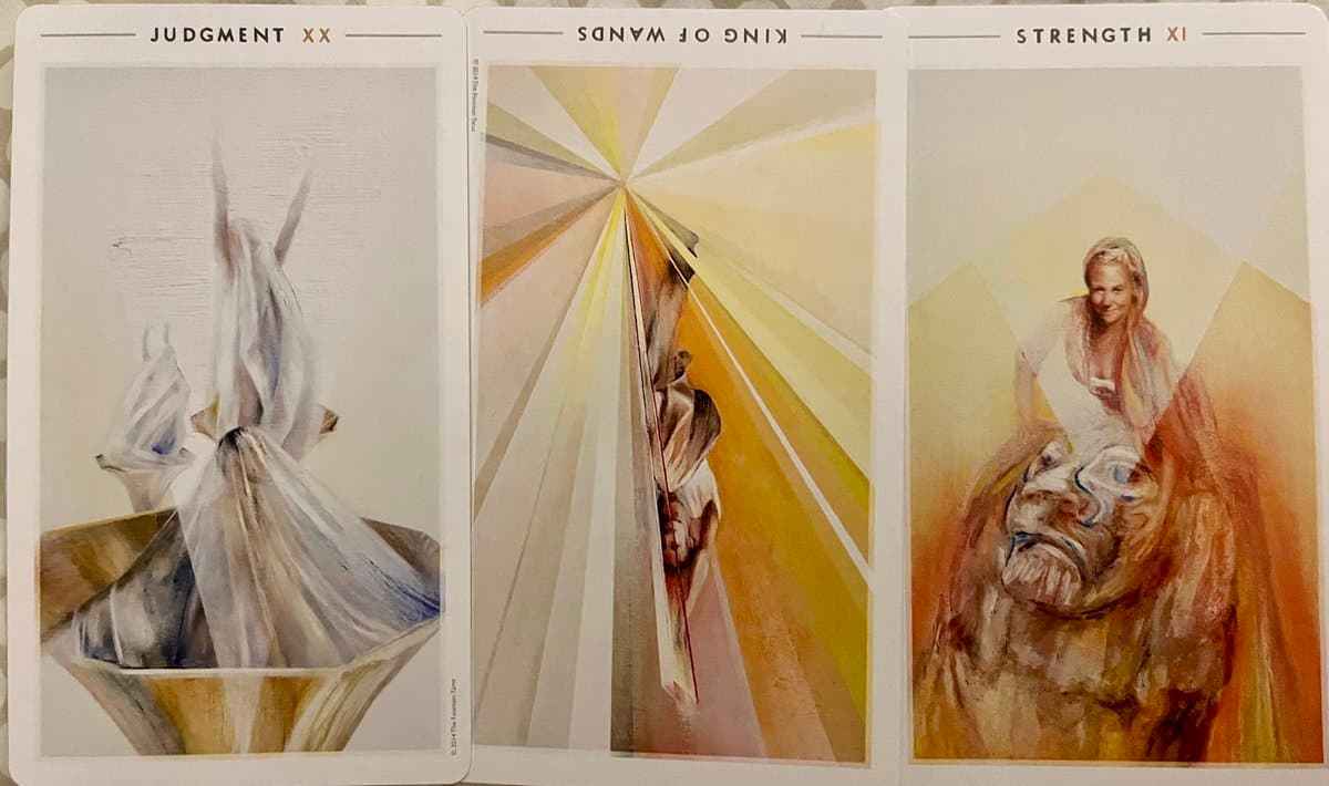 A photograph of three tarot cards laid side-by-side, featuring the cards Judgement, King of Wands, and Strength.