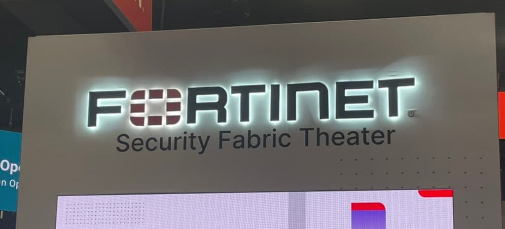 A photo of a large, illuminated sign at an event or conference. The sign displays the Fortinet logo and the text "Security Fabric Theater" on a metallic panel.