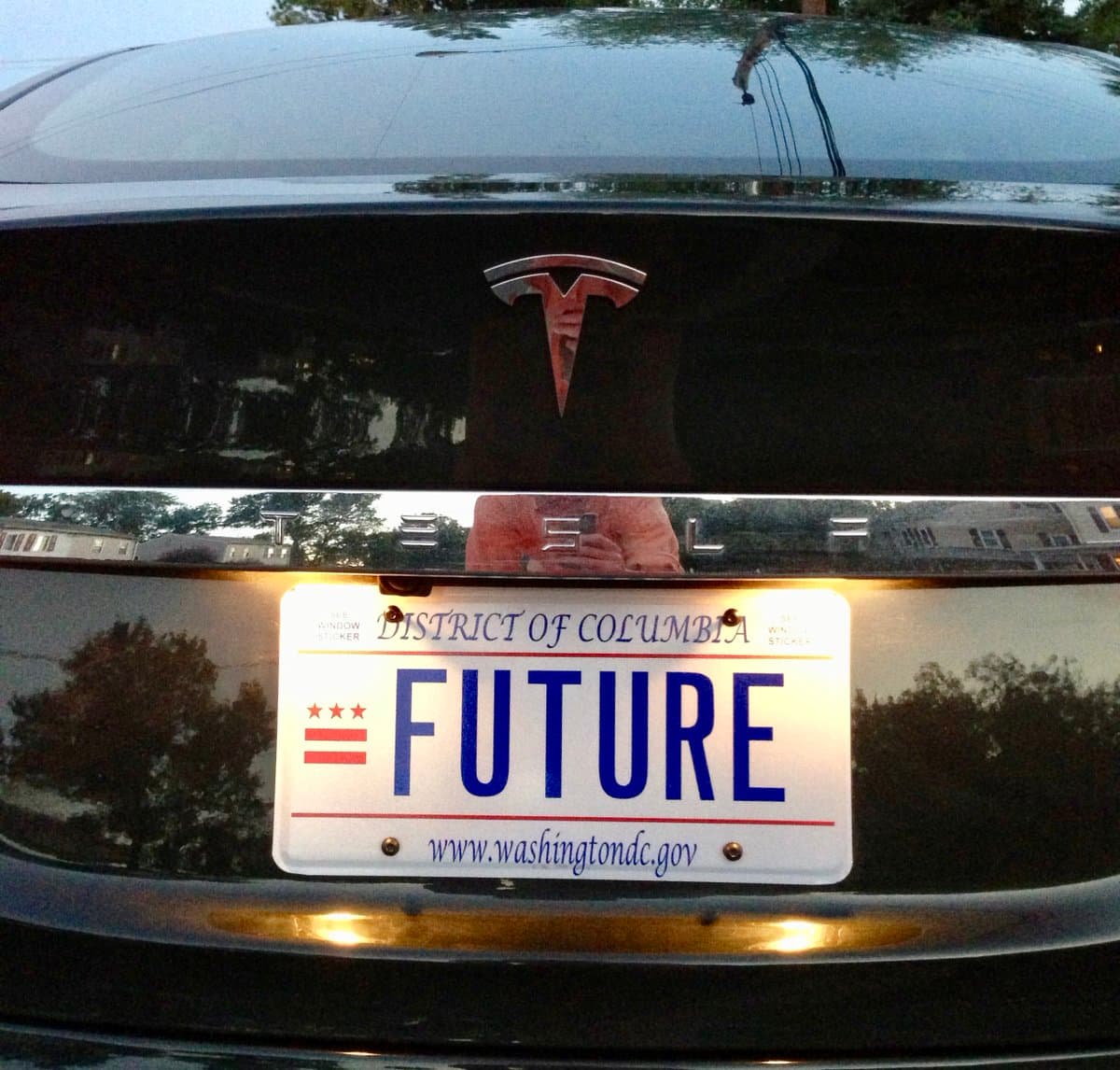 A close-up photograph of the rear of a black Tesla vehicle, featuring a District of Columbia license plate with the word 'FUTURE' in large blue letters.