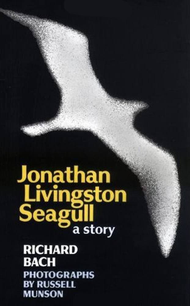 A book cover for 'Jonathan Livingston Seagull: a story' by Richard Bach, featuring a stylized white seagull in flight against a black background. The title is printed in yellow and white text, with credits for photographs by Russell Munson at the bottom.