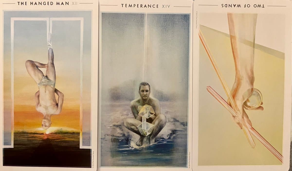 A photograph of three tarot cards laid side-by-side: The Hanged Man, Temperance, and Two of Wands.