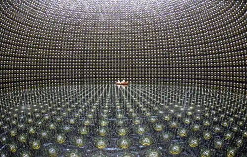 A wide-angle photograph of the interior of a large, spherical scientific detector, featuring thousands of glass spheres arranged in a grid pattern on the walls and floor. A small, white, boat-shaped object sits in the center of the floor.