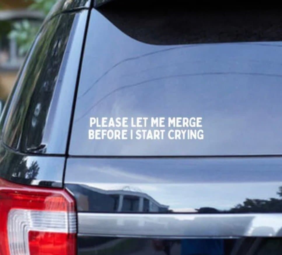A close-up photograph of the rear window of a dark-colored vehicle, featuring a white text decal. The image is a humorous meme referencing software development frustrations.