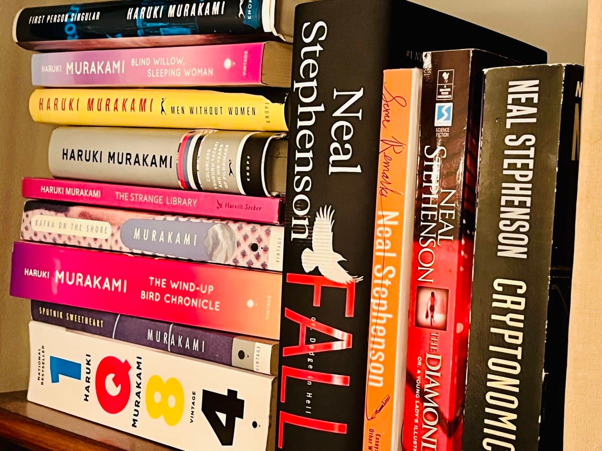 A close-up photograph of a bookshelf displaying a collection of novels, primarily by Haruki Murakami and Neal Stephenson. The books are arranged vertically, with their spines facing forward, showing various titles and authors.