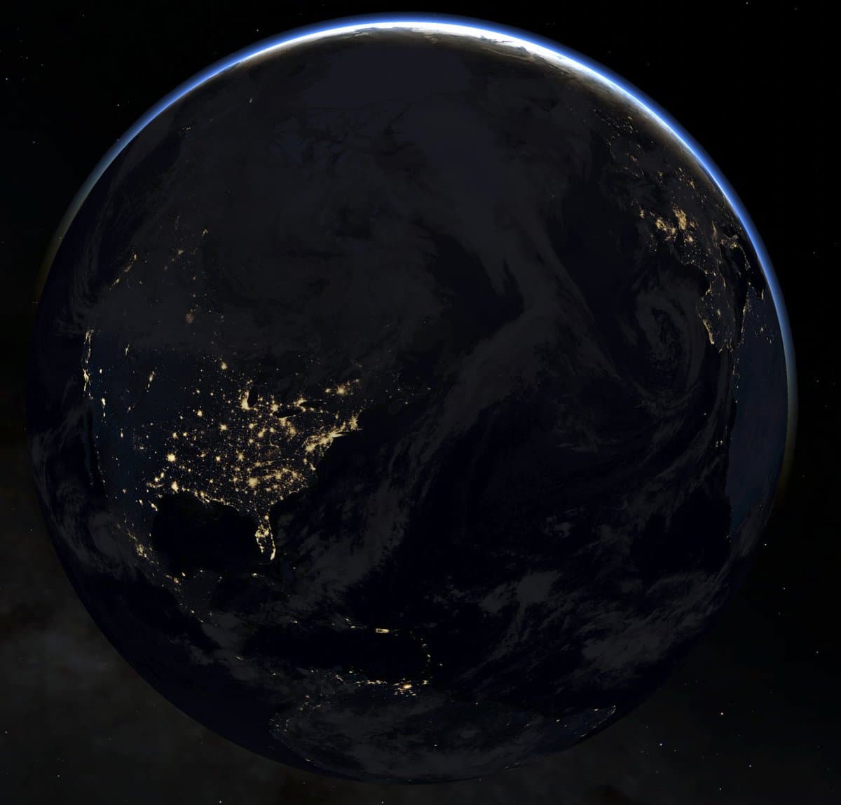 A photograph of Earth at night taken from space, showing the illuminated city lights of East Asia against the dark planet surface. A thin blue line of the atmosphere glows along the upper edge of the globe against the blackness of space.