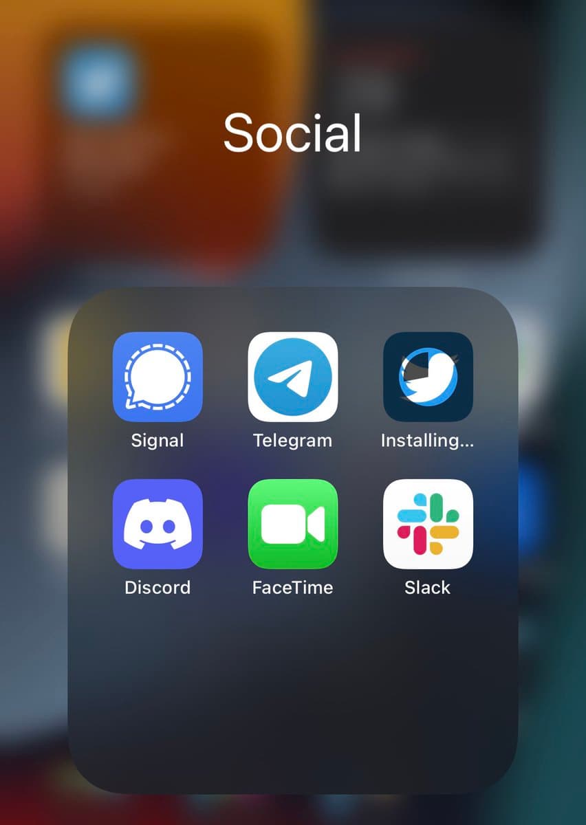 A screenshot of a smartphone's home screen showing a folder labeled "Social" containing app icons for Signal, Telegram, Discord, FaceTime, and Slack, with a Twitter icon in the process of installing.