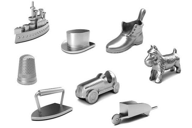A collection of eight silver-colored metal trinkets shaped like classic Monopoly game pieces, including a battleship, top hat, boot, thimble, dog, car, iron, and wheelbarrow, arranged on a white background.