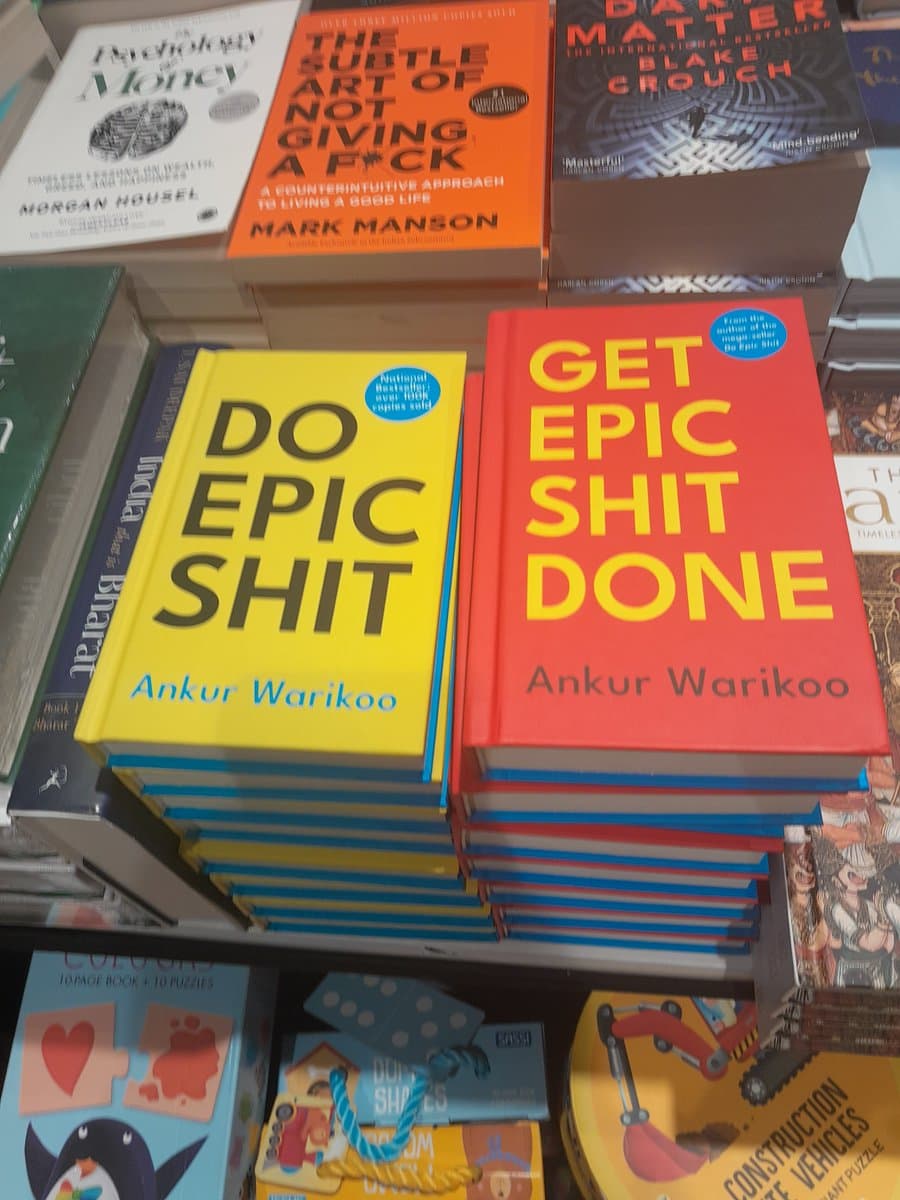 A photograph of a bookstore display featuring stacks of self-help books, prominently showing copies of "Do Epic Shit" and "Get Epic Shit Done" by Ankur Warikoo. Other visible titles include "The Subtle Art of Not Giving a F*ck" by Mark Manson and "Psychology of Money" by Morgan Housel.