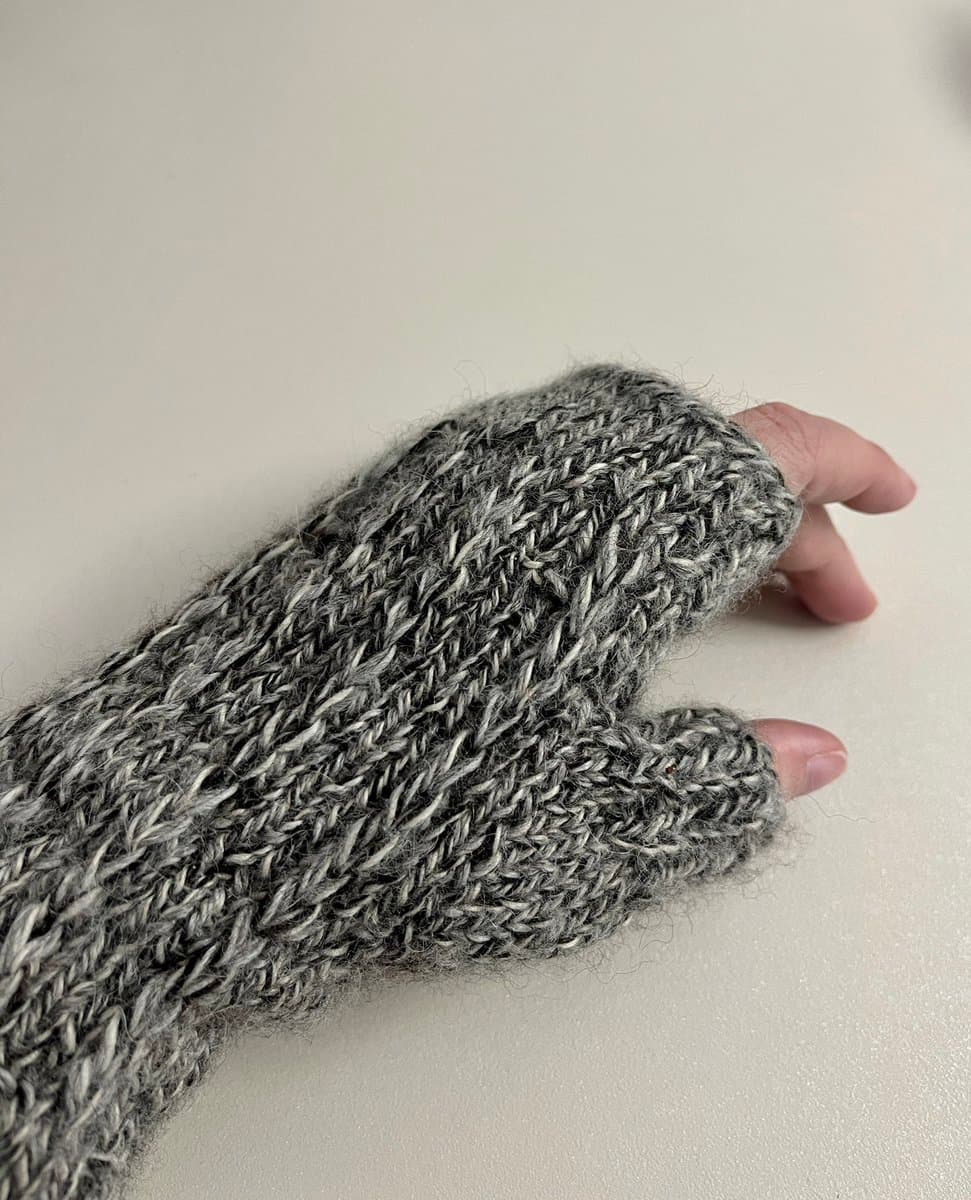 A close-up photograph of a hand wearing a gray, knitted fingerless glove against a plain white background.