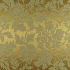 A close-up view of a patterned fabric featuring a dense, repeating floral and foliate design in shades of gold and olive green. The texture appears to be a woven textile, likely a brocade or damask, with a subtle sheen.
