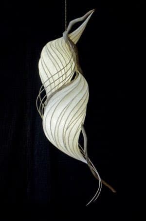 A hanging light fixture with an organic, twisted form made of white, ribbed material against a black background. The design features flowing, wave-like curves and thin, wire-like elements extending from the top and bottom.