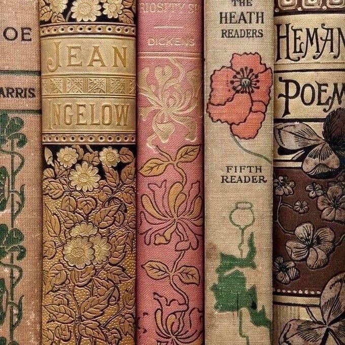 A close-up photograph of the spines of several vintage books arranged side-by-side, featuring ornate floral and botanical designs in gold, pink, and brown tones. The books display classic typography and decorative patterns typical of older editions. The image highlights the tactile and aesthetic qualities of the book covers and spines.