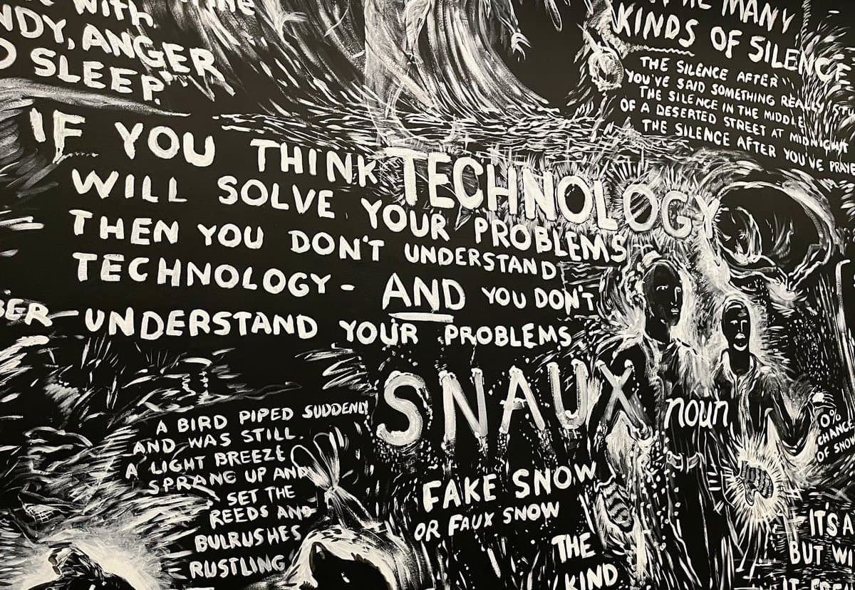 A black and white hand-painted mural featuring expressive white text and illustrations on a dark background. The artwork includes a central quote about technology, a definition of the word 'SNAUX,' and a section titled 'Kinds of Silence' accompanied by figures and nature imagery.