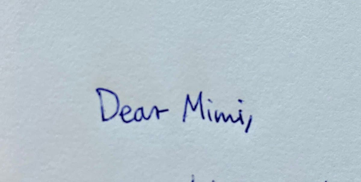 A close-up photograph of a handwritten letter on white paper. The visible text is written in blue ink and reads "Dear Mimi,".