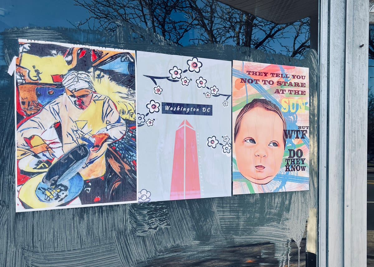 Three hand-drawn posters are taped to a glass window. The left poster depicts a person in a white head wrap and coat, the middle poster shows a pink obelisk with flowers and the text 'Washington DC', and the right poster features a baby's face with the text 'THEY TELL YOU NOT TO STARE AT THE SUN BUT WTF DO THEY KNOW'.
