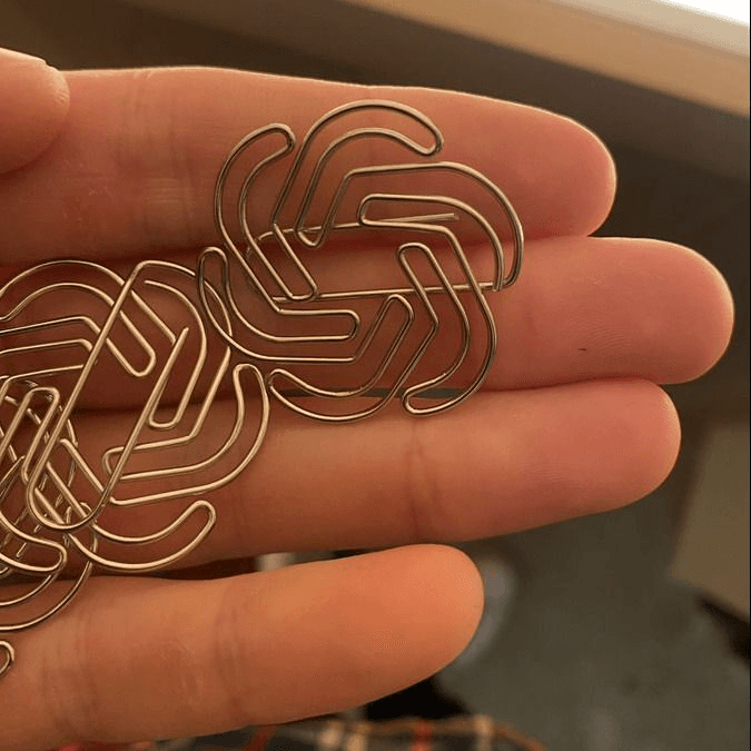 A close-up photograph of a person's open palm holding several small, metallic, wire-bent objects that resemble the OpenAI logo. The objects are arranged in a cluster on the fingers, with a blurred indoor background.