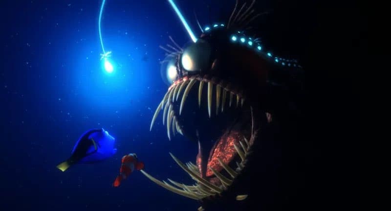 A digital illustration depicting a deep-sea scene where a large, menacing anglerfish with glowing bioluminescent lures and sharp teeth looms over a blue tang and a clownfish. The background is a dark blue ocean with light particles suspended in the water.