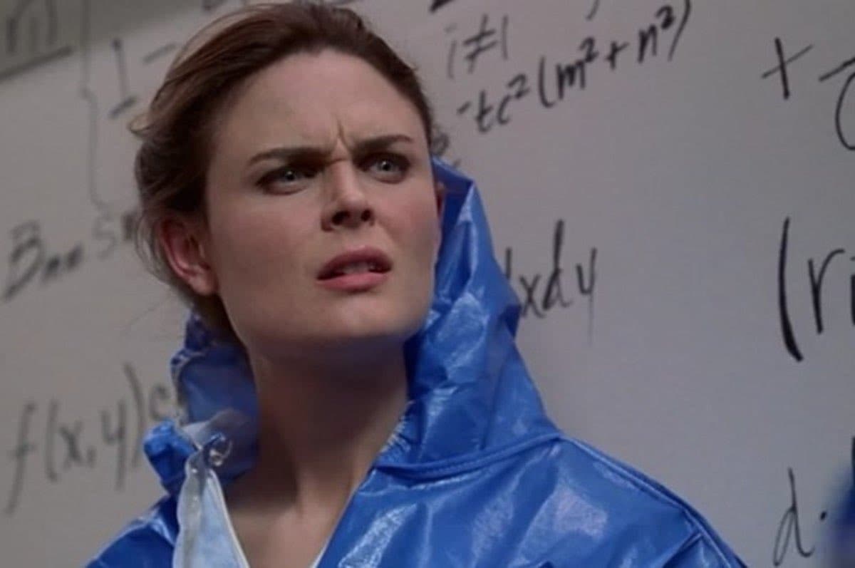 A woman wearing a blue rain poncho stands in front of a whiteboard covered in handwritten mathematical equations and symbols, looking off to the side with a concerned expression. The image appears to be a still from a film or television show.