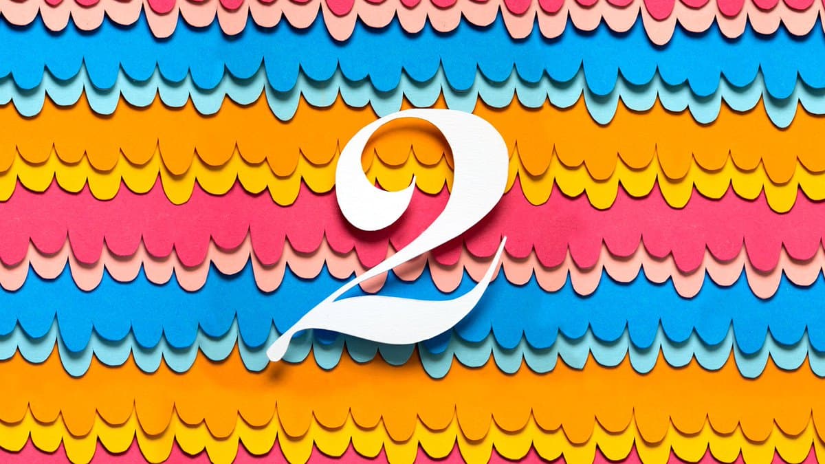 A colorful, abstract image featuring a large white number 2 centered against a background of horizontal, scalloped paper-cut strips in shades of blue, orange, yellow, and pink.