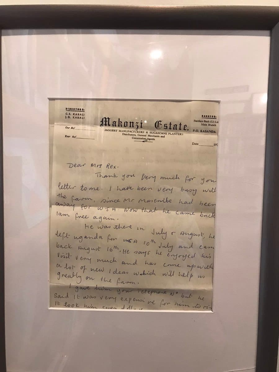 A framed, handwritten letter on Makonzi Estate letterhead, displayed in a glass case. The letter is addressed to Mrs. Rex and discusses farm activities and a visitor's trip to Uganda.