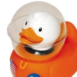 A close-up photograph of a white rubber duck with an orange beak, wearing a clear plastic astronaut helmet and an orange spacesuit with a small American flag patch on the chest.