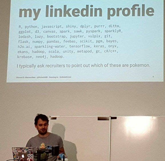 A photo of a man giving a presentation in front of a large screen displaying a humorous LinkedIn profile. The profile lists programming languages and libraries alongside Pokémon names, with a punchline about recruiters not knowing the difference.