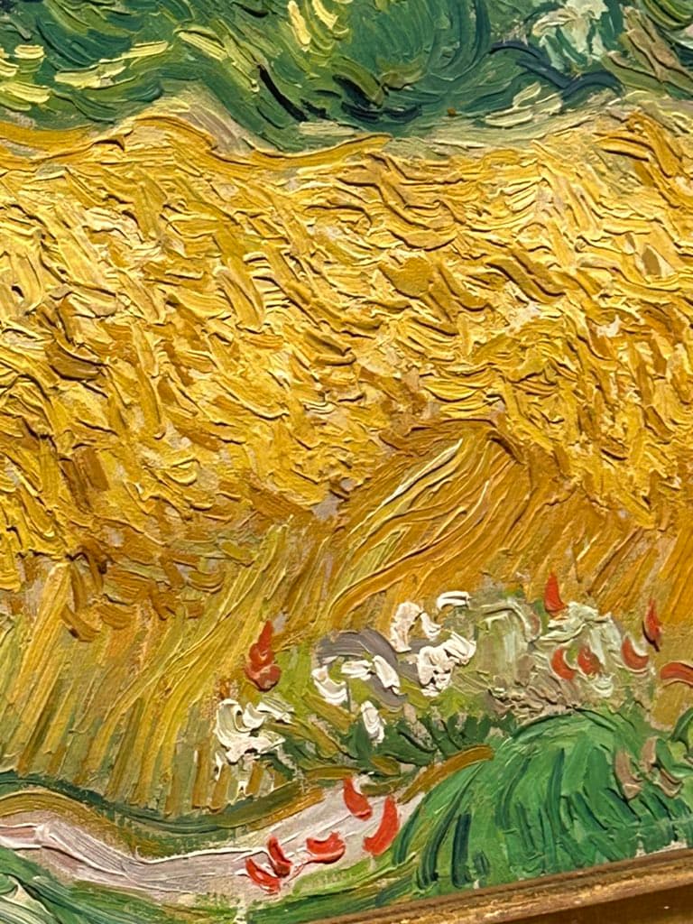 A close-up photograph of an oil painting featuring thick, textured brushstrokes in shades of yellow, green, and white, with small red accents.