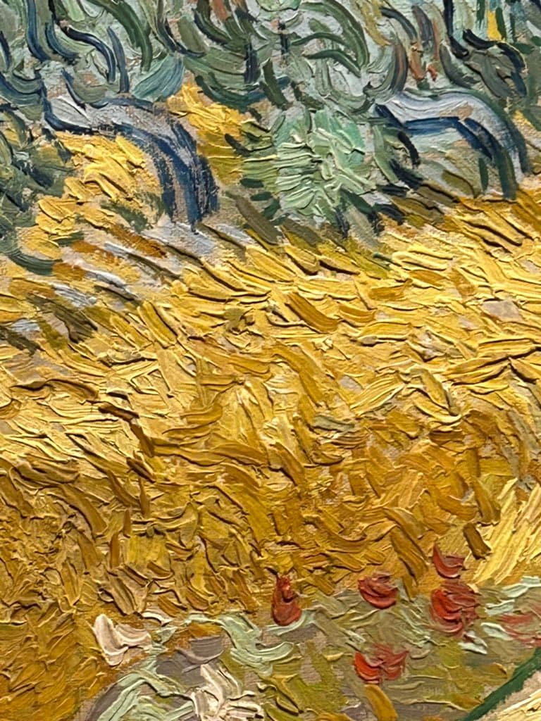 A close-up photograph of a painting featuring thick, textured impasto brushstrokes in shades of yellow, green, and blue, with small red accents near the bottom.