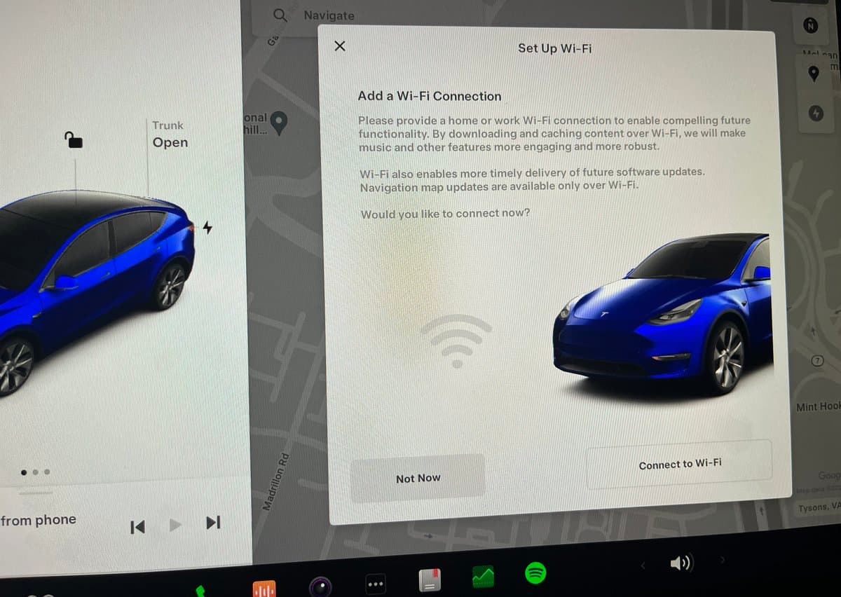 A photograph of a car's central touchscreen displaying a pop-up prompt to set up a Wi-Fi connection. The screen shows a blue Tesla Model Y and text explaining the benefits of connecting to Wi-Fi, with options to 'Connect to Wi-Fi' or 'Not Now'.