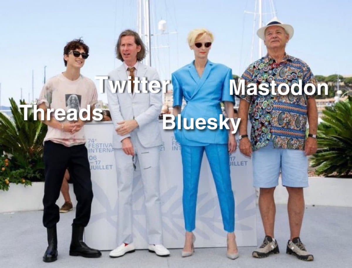 A meme featuring a photo of four people standing in a row at an outdoor event, with text labels overlaid on each person to represent different social media platforms.