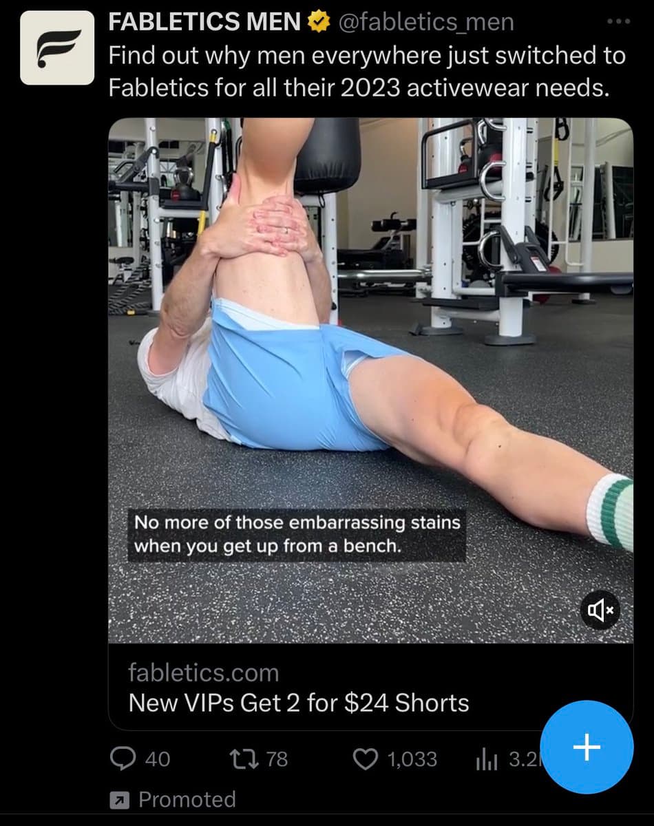A screenshot of a promoted tweet from the account @fabletics_men. The tweet features a video of a man in blue shorts performing a leg stretch on a gym floor, with a caption about avoiding stains. The ad includes a call to action for a discount on shorts.