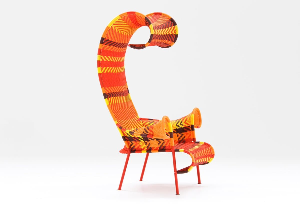A studio photograph of a modern armchair featuring a tall, curved backrest and a vibrant orange, yellow, and black geometric pattern on a white background.