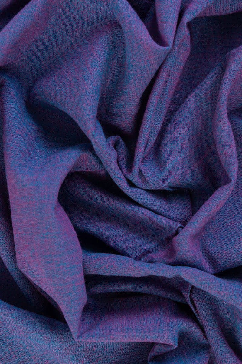 A close-up photograph of crumpled, textured fabric in shades of purple and blue. The material features a subtle, woven pattern with small flecks of color, creating a soft and organic appearance.