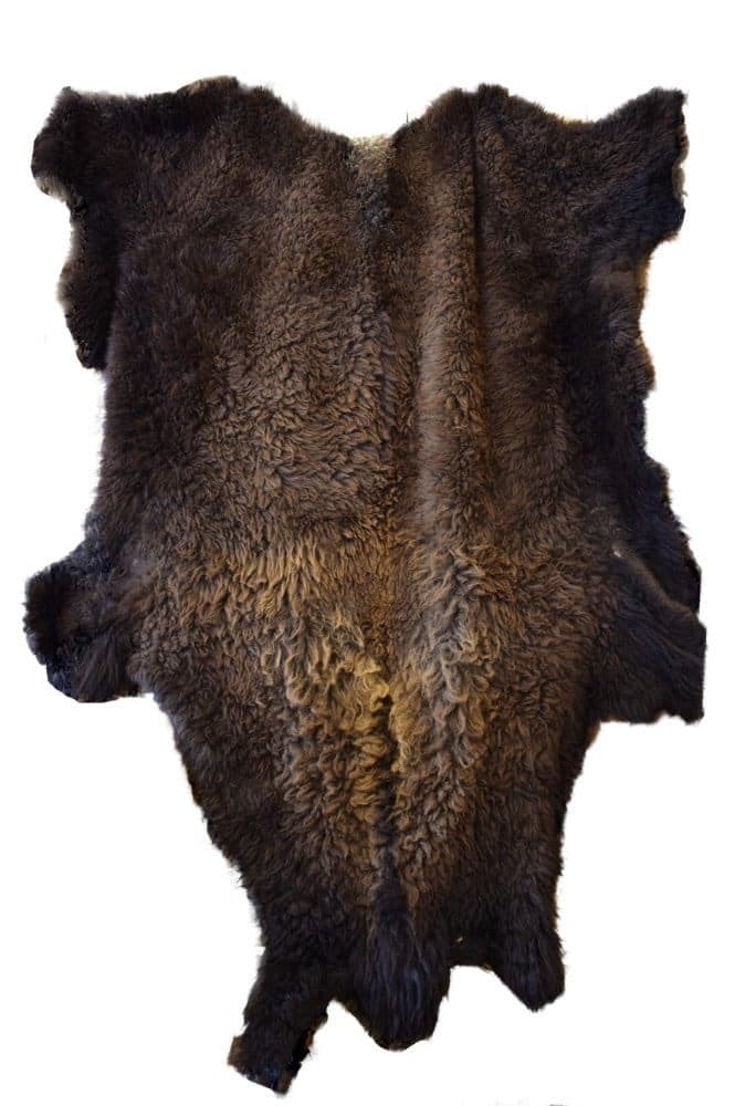 A full animal pelt with thick, curly brown fur is displayed flat against a plain white background. The pelt is spread out to show its full shape, including the head, legs, and tail.