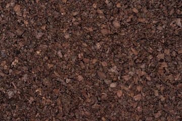A close-up, full-frame photograph of dark brown, granular soil or mulch. The texture is coarse and uneven, with small pebbles and organic matter visible throughout.
