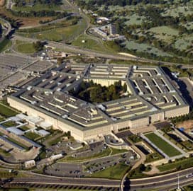 An aerial photograph of the Pentagon building, showing its distinctive five-sided structure and surrounding parking lots and roads.