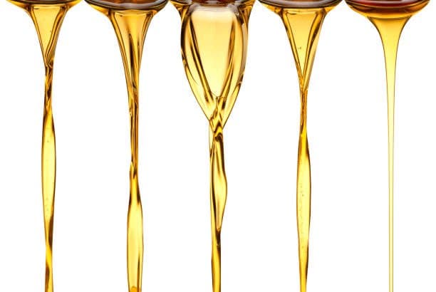 A close-up photograph of five streams of golden, viscous liquid pouring downward against a white background. The liquid appears to be honey or a similar syrup, with varying thickness and flow patterns in each stream.