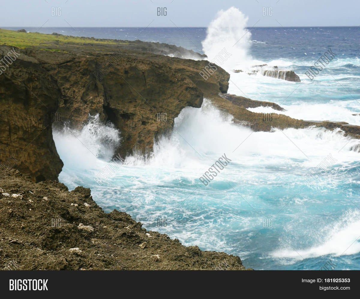 A stock photograph showing powerful ocean waves crashing against a rugged, brown coastal cliff, creating a large spray of white water. The image features a 'BIGSTOCK' watermark overlay and a footer bar with image identification details.